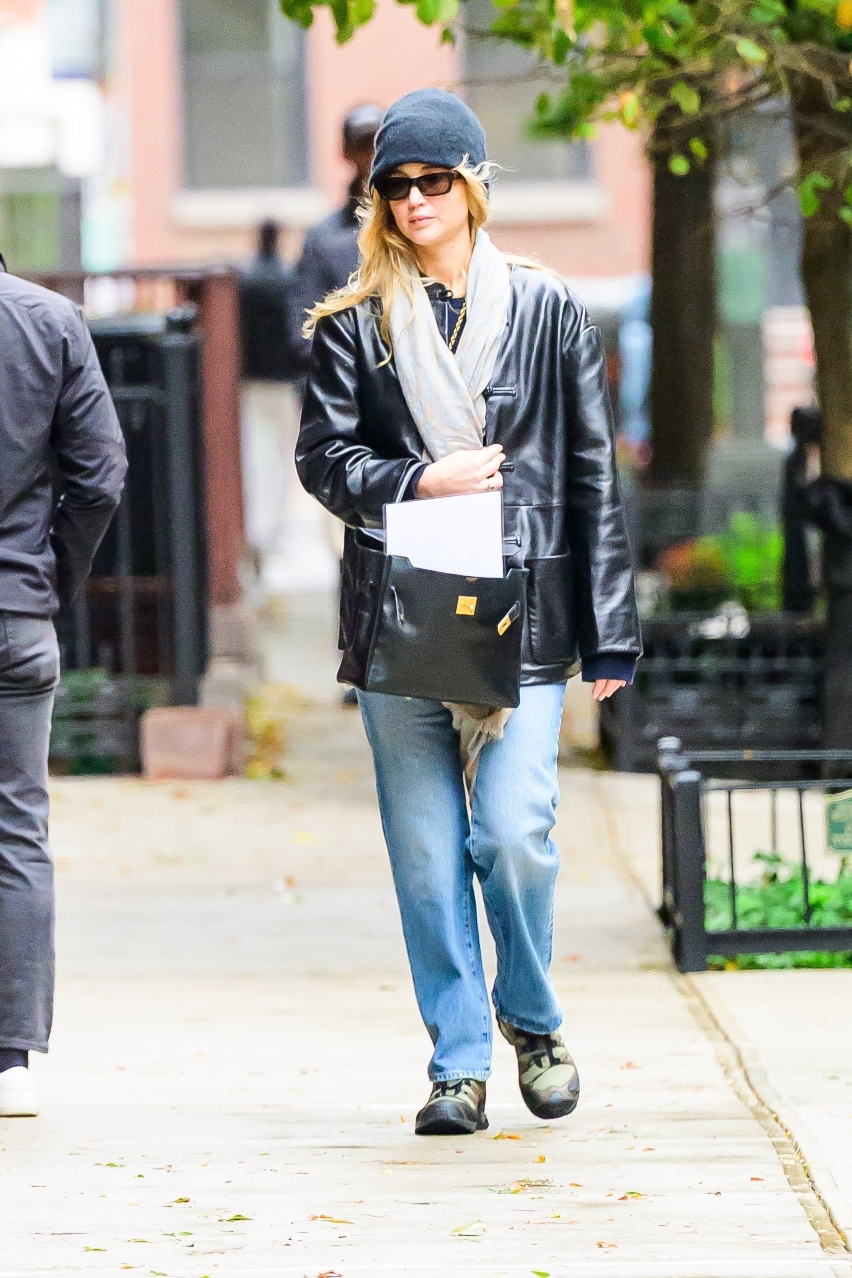 J.law wears a gray beanie, gray scarf, leather jacket, jeans, and Salomon sneakers.