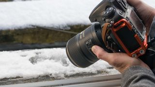 Man holding Nikon D800 and Nikon 105mm macro lens next to a snow-covered window sill