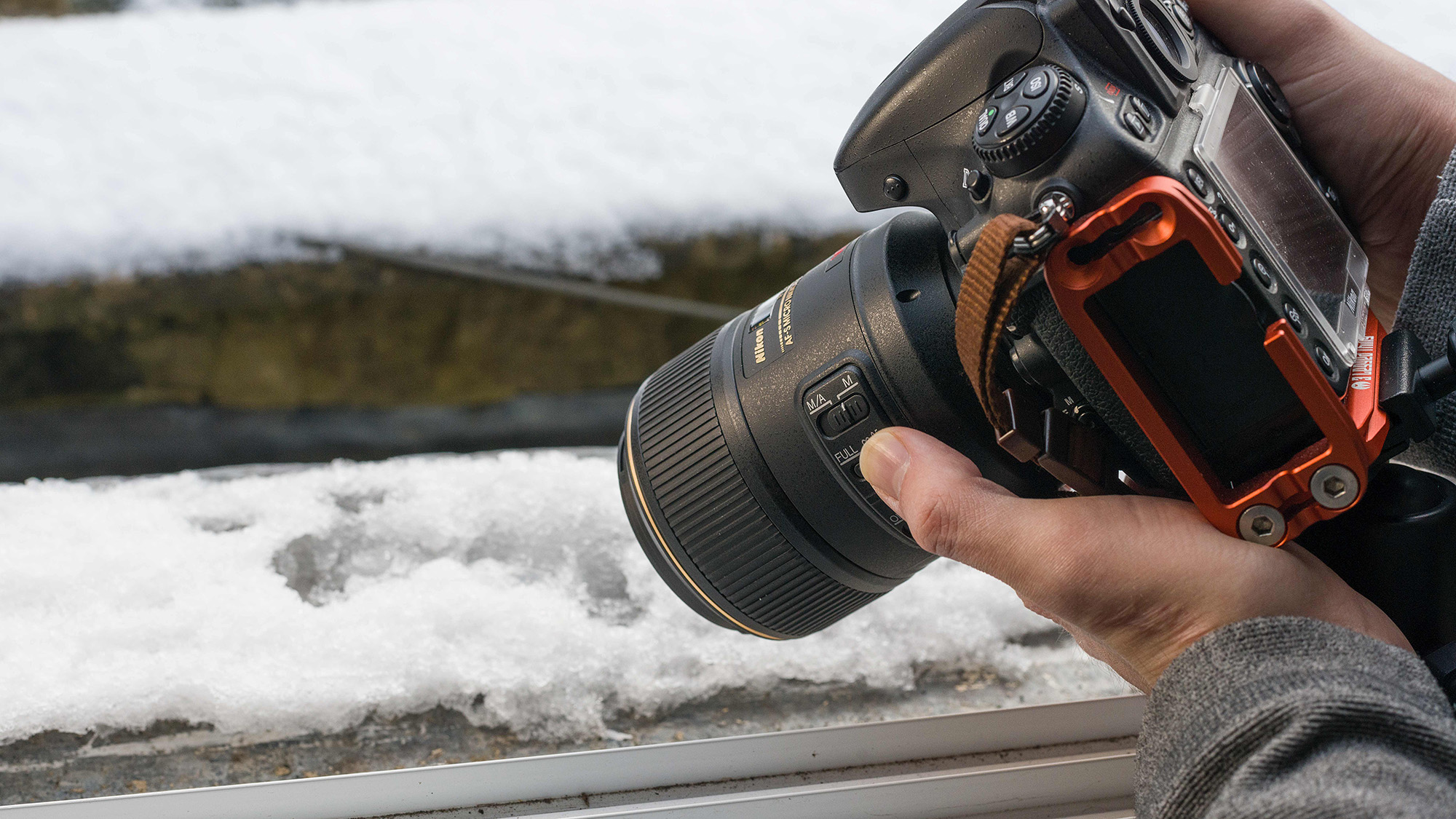 Man holding Nikon D800 and Nikon 105mm macro lens next to a snow-covered window sill