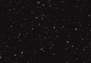 hundreds of galaxies of different colors appear tiny in a wide view of deep space