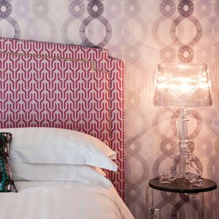 bedroom with pink designed wallpaper with bed with cushion and lamp