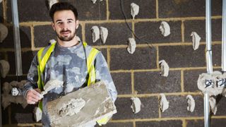 Plasterer with trowel and hawk stood in front of block wall