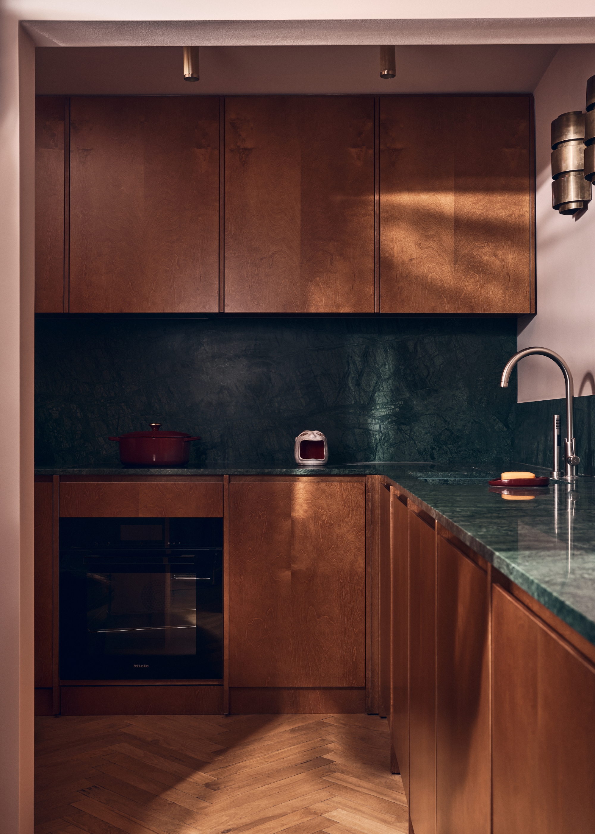 A golden wood kitchen with a dark green marble countertop and pink walls