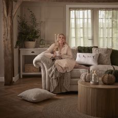 Stacey Solomon sat on cream sofa with homeware collection around her.