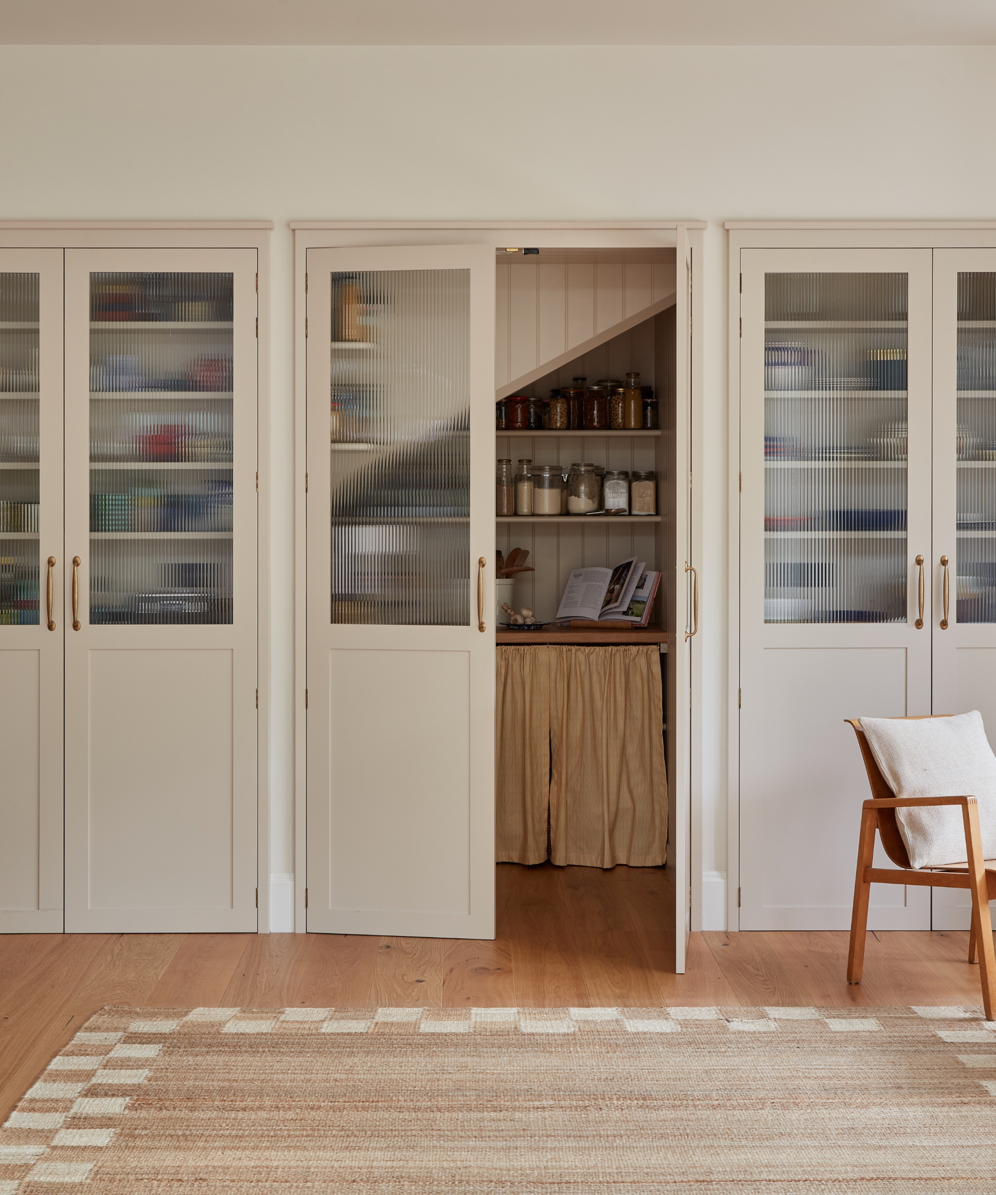 A large pantry installed below the stairs, with white and ribbed glass doors