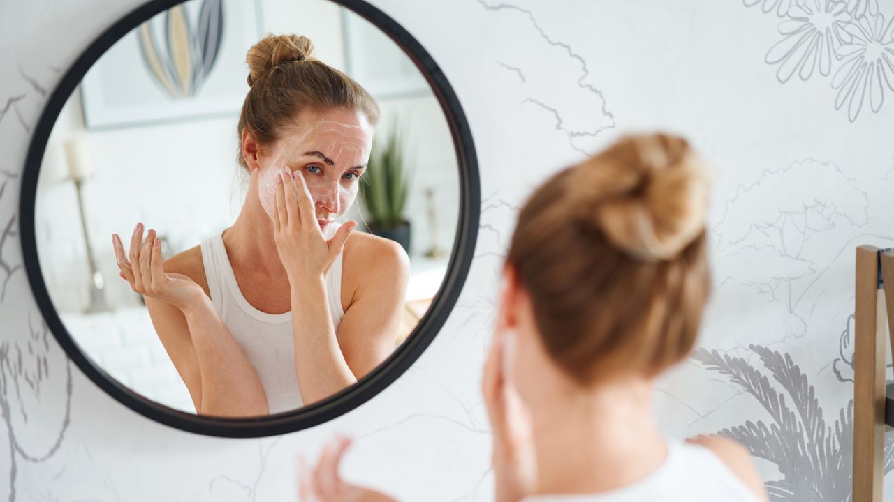 Woman washing her face in the mirror, stock photo 