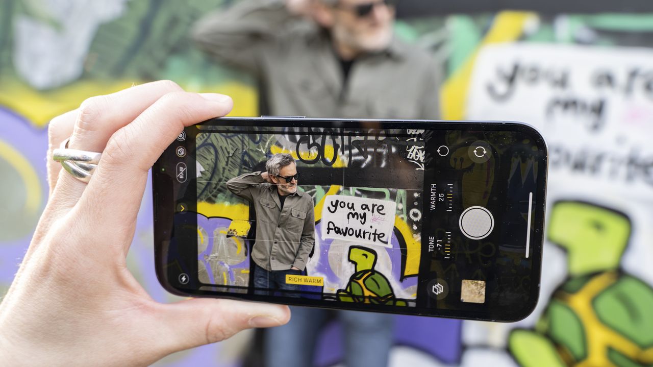 A phone screen showing a man standing in front of graffiti