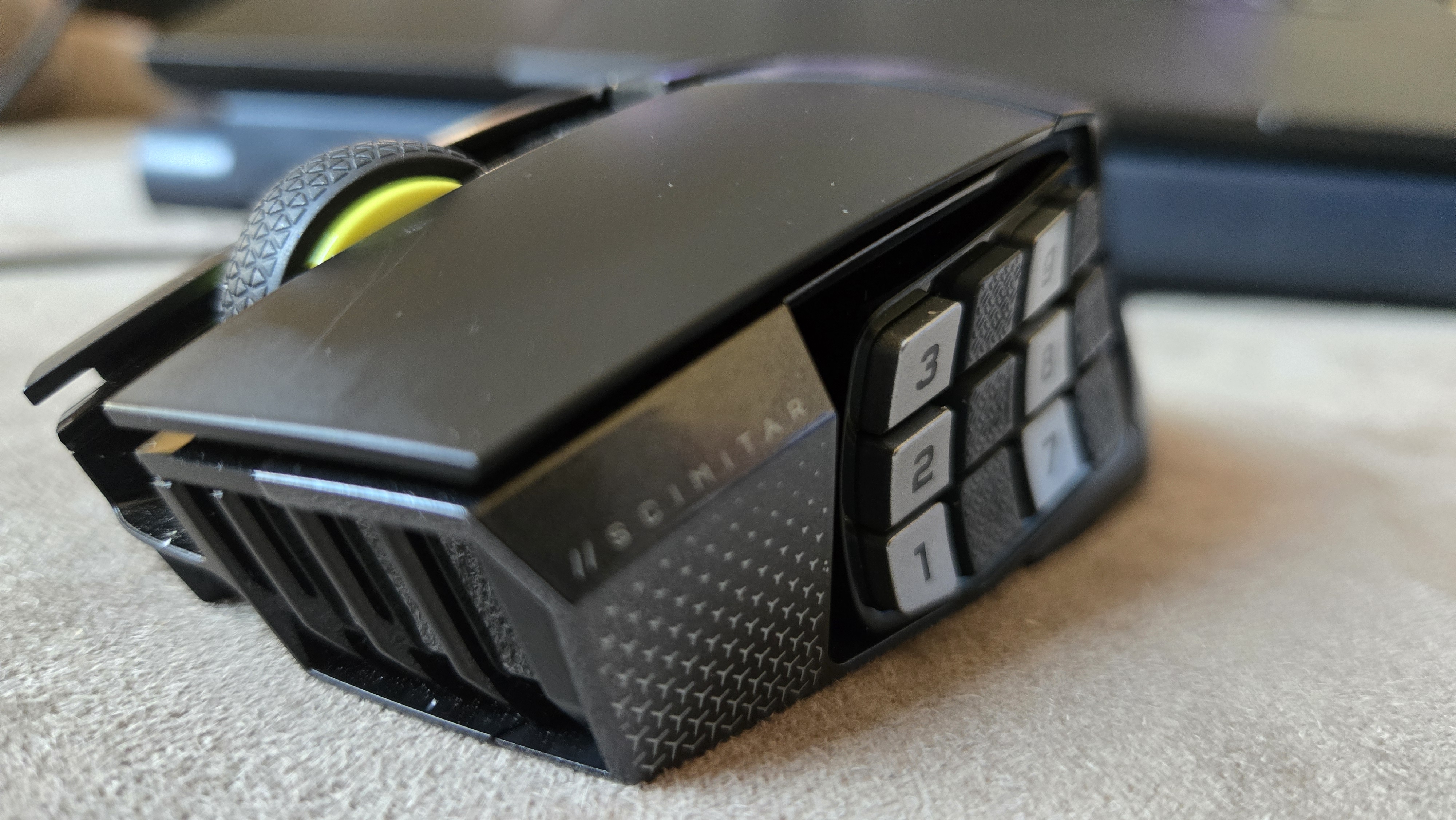 A Corsair Scimitar Elite Wireless SE gaming mouse on a carpet next to a gaming laptop and Stream Deck.