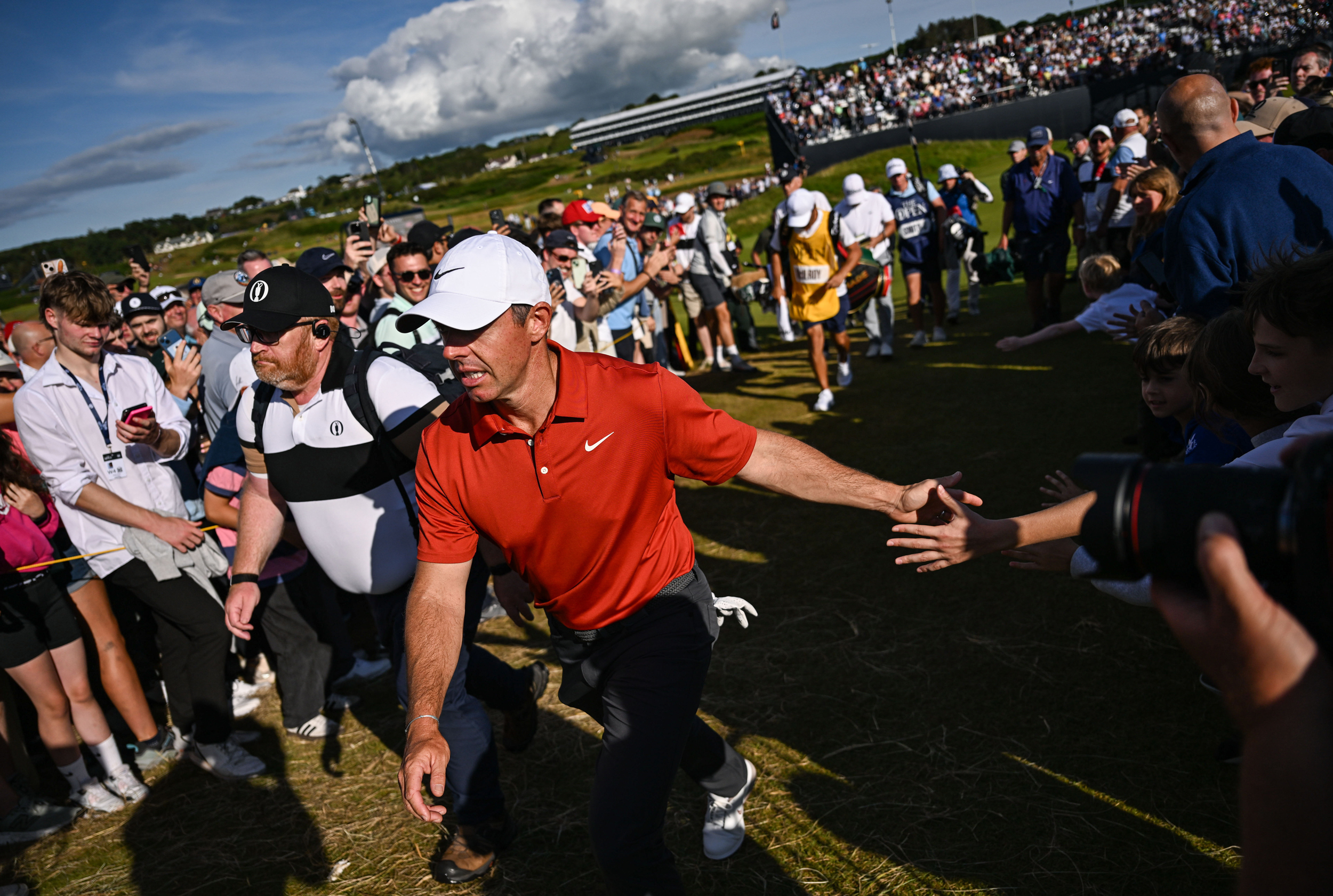 Rory McIlroy low-fives fans walking between a green and tee box at Royal Portrush during round three