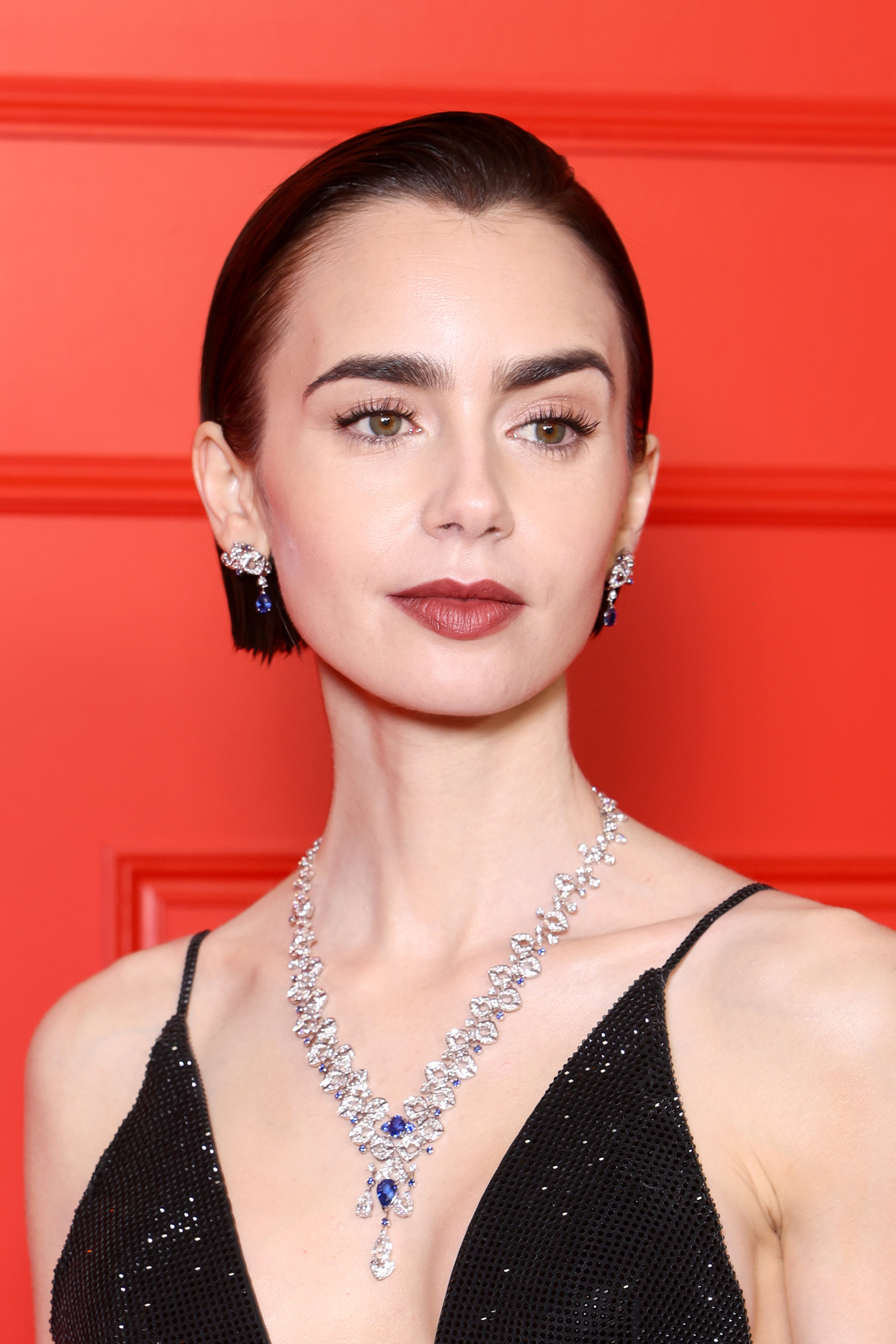 a close-up red carpet photo of a white woman with short, dark hair. she is wearing a black gown with a plunging neckline and a silver diamond necklace