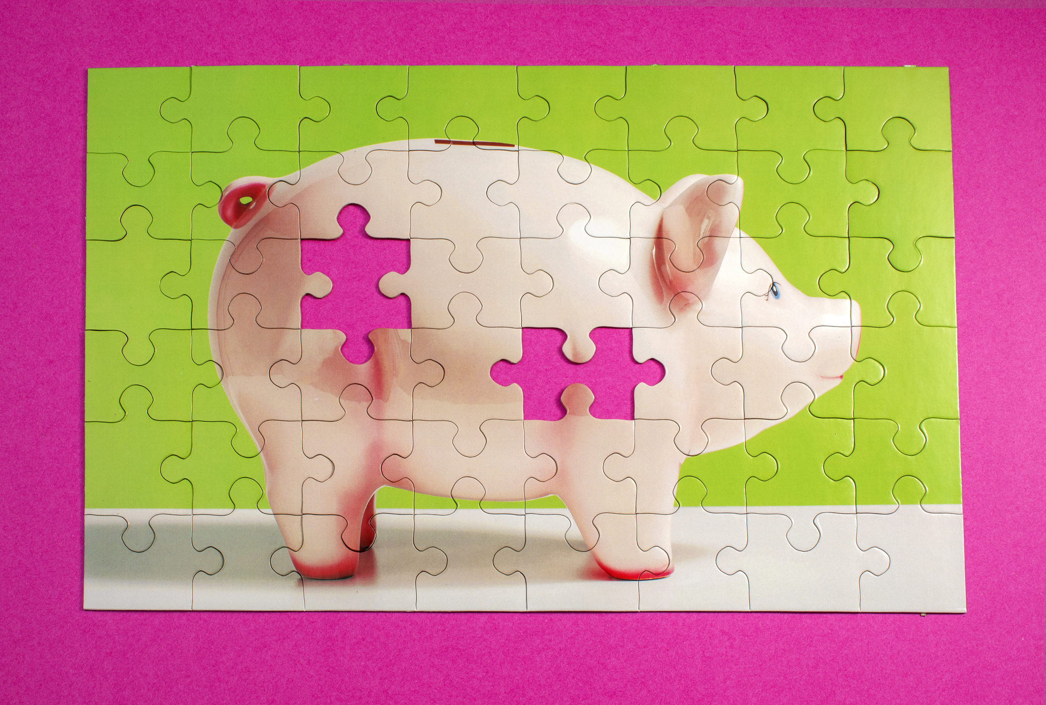 Jigsaw puzzle of pink ceramic piggy bank with 2 pieces missing, pink surface, high angle view