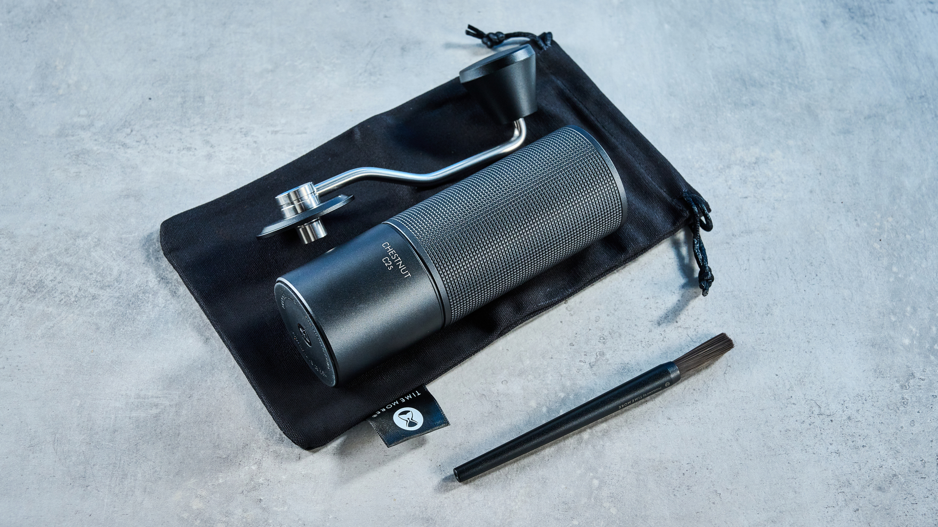 the timemore chestnut c2s coffee grinder in black showing its hand crank and catch chamber photographed against the blue tom's guide background