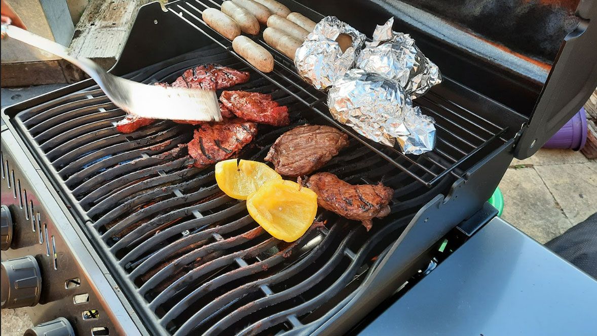 Image shows food including corn, steaks and sausages grilling on the Napoleon Freestyle 425.