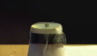 The magnetic cube hovers in the air as liquid nitrogen flows around the superconductor beneath the cube.