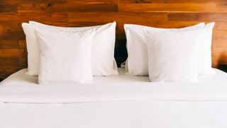 Six white pillows on a white bed with a wooden backboard