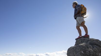 A man with a backpack stands on the top of a mountain looking down.