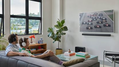 Two men in a brightly lit apartment listening to what looks like Formula 1 racing on their Sonos Ace headphones