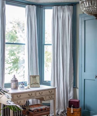bay window in a bedroom with blue painted woodwork and antique dressing table
