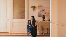 Young Huh sits on a chair in a cream entryway looking dreamily away from the camera and off the side