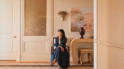 Young Huh sits on a chair in a cream entryway looking dreamily away from the camera and off the side