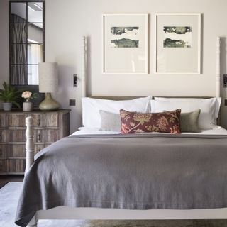 White bedroom with artwork above the bed and a framed mirror above the chest of drawers