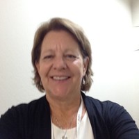 a headshot photo of therapist Patricia Bathurst: a lady with a brown bob in a white top and black long sleeved cardigan smiling at the camera