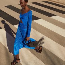 Model wearing blue two piece set and accessories sold at The Outnet walking across a zebra crossing