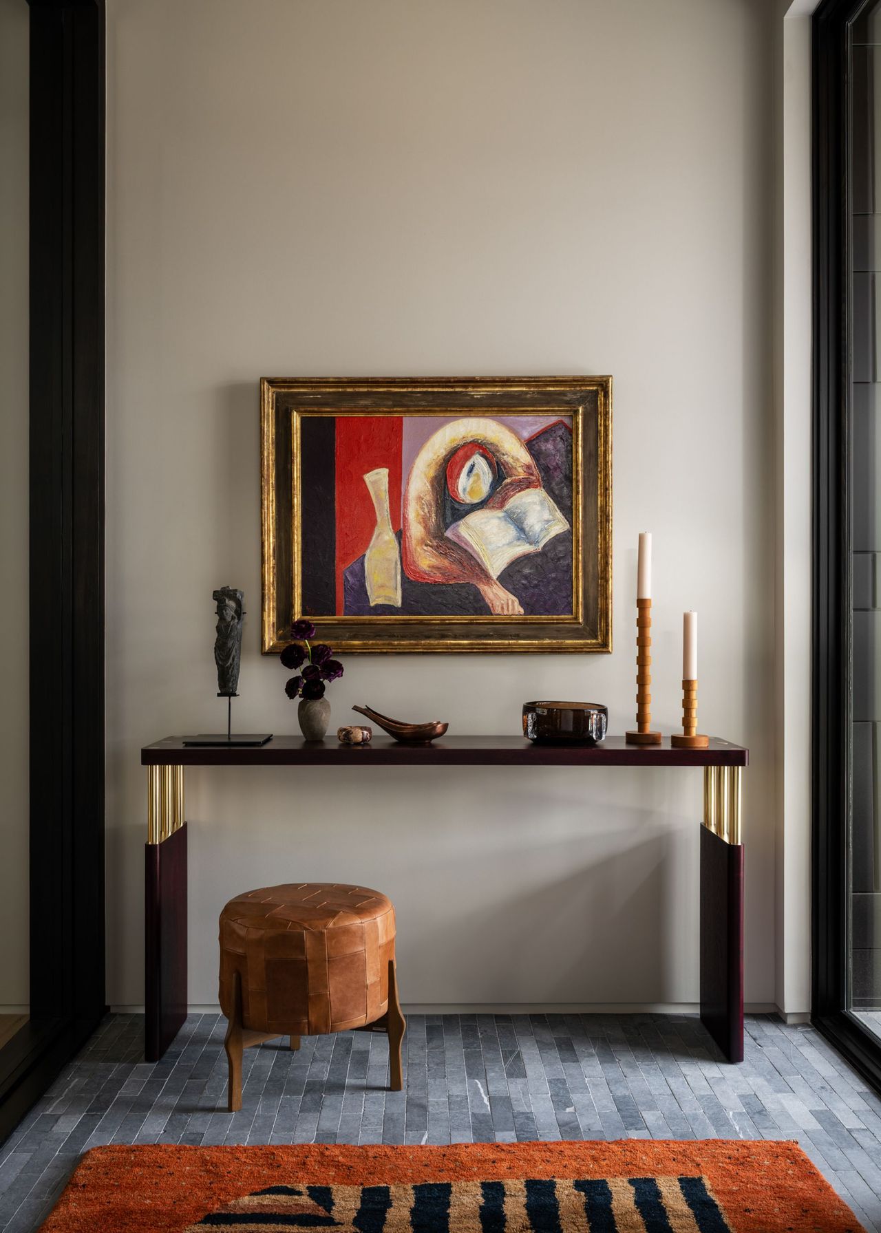 A console table below a piece of art with decorative details on top and a rug that has similar tones to the painting lies on the floor in front
