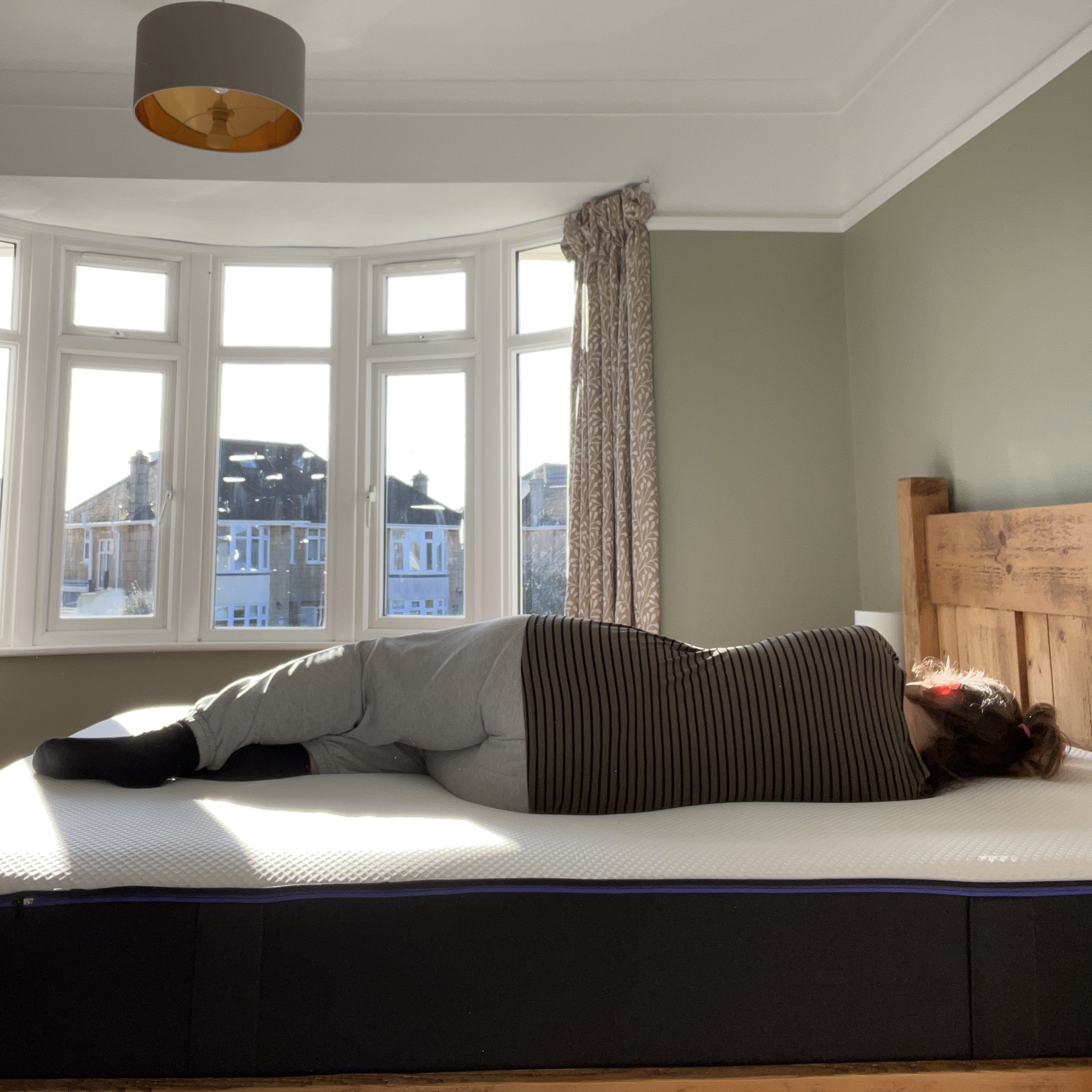 A woman lying on her side on the Nectar Premier Hybrid Mattress in front of a bay window in a bedroom