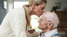 Woman kissing elderly father on the head at home