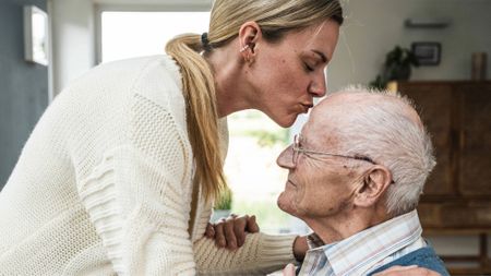 Woman kissing elderly father on the head at home