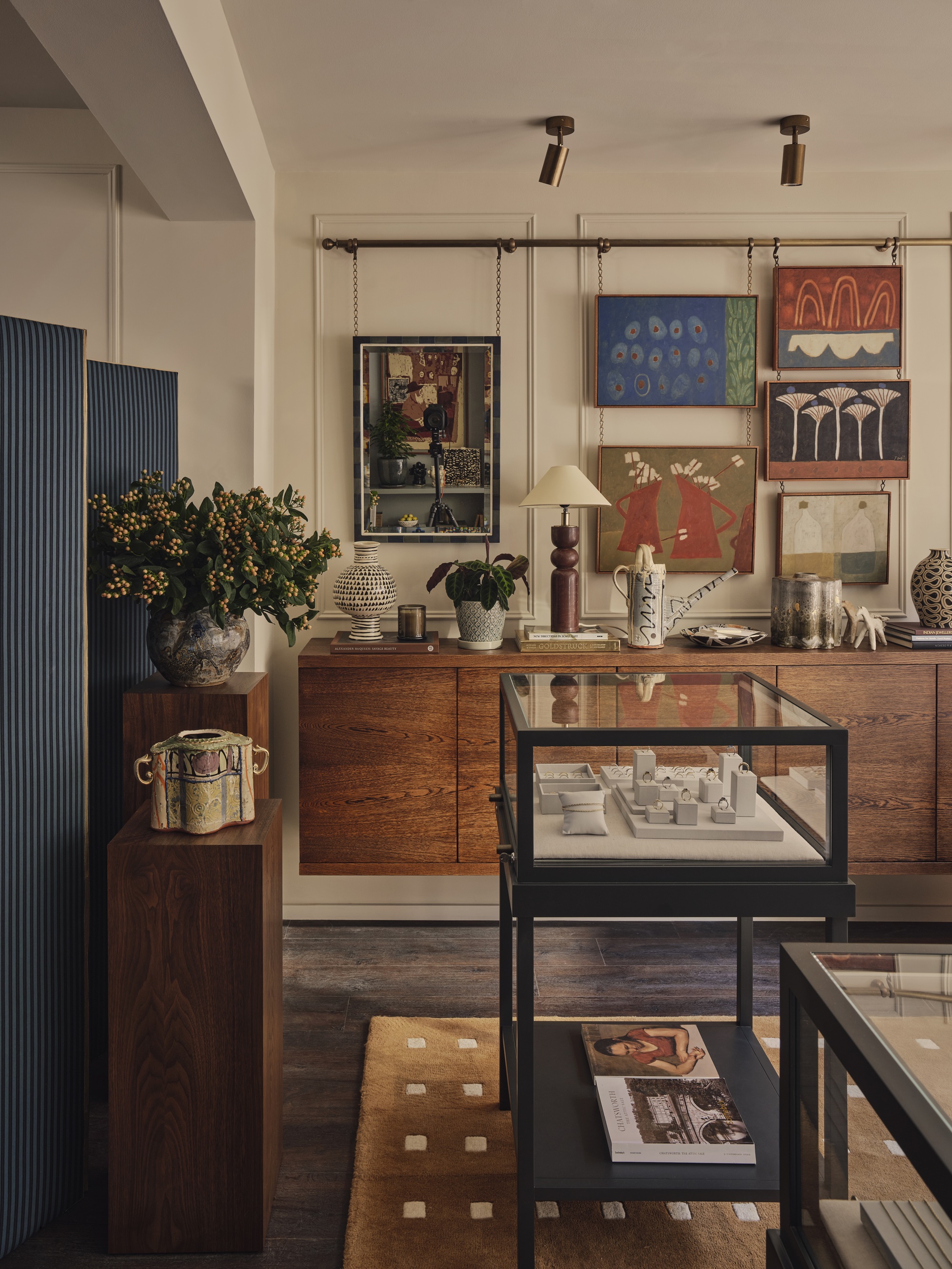 jewellery store with floating timber console, artworks hanging from picture rail on chains, a glass cabinet with rings, and a mustard yellow rug