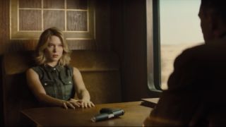 Léa Seydoux sits in front of Daniel Craig, with a gun between them, in Spectre.