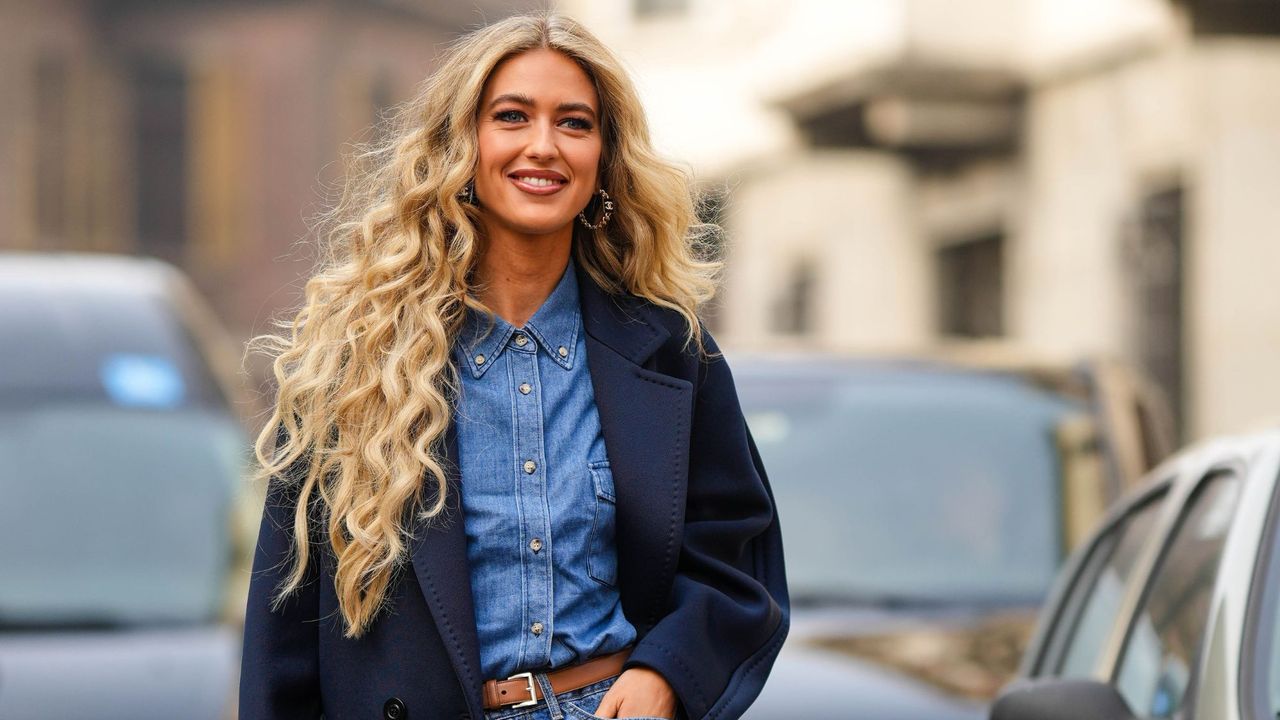 woman with big curly hair walks down the street smiling - gettyimages 1469088128