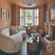 A colour-drenched narrow living room with a curved sofa in off-white boucle and an organic-shaped marble-topped coffee table