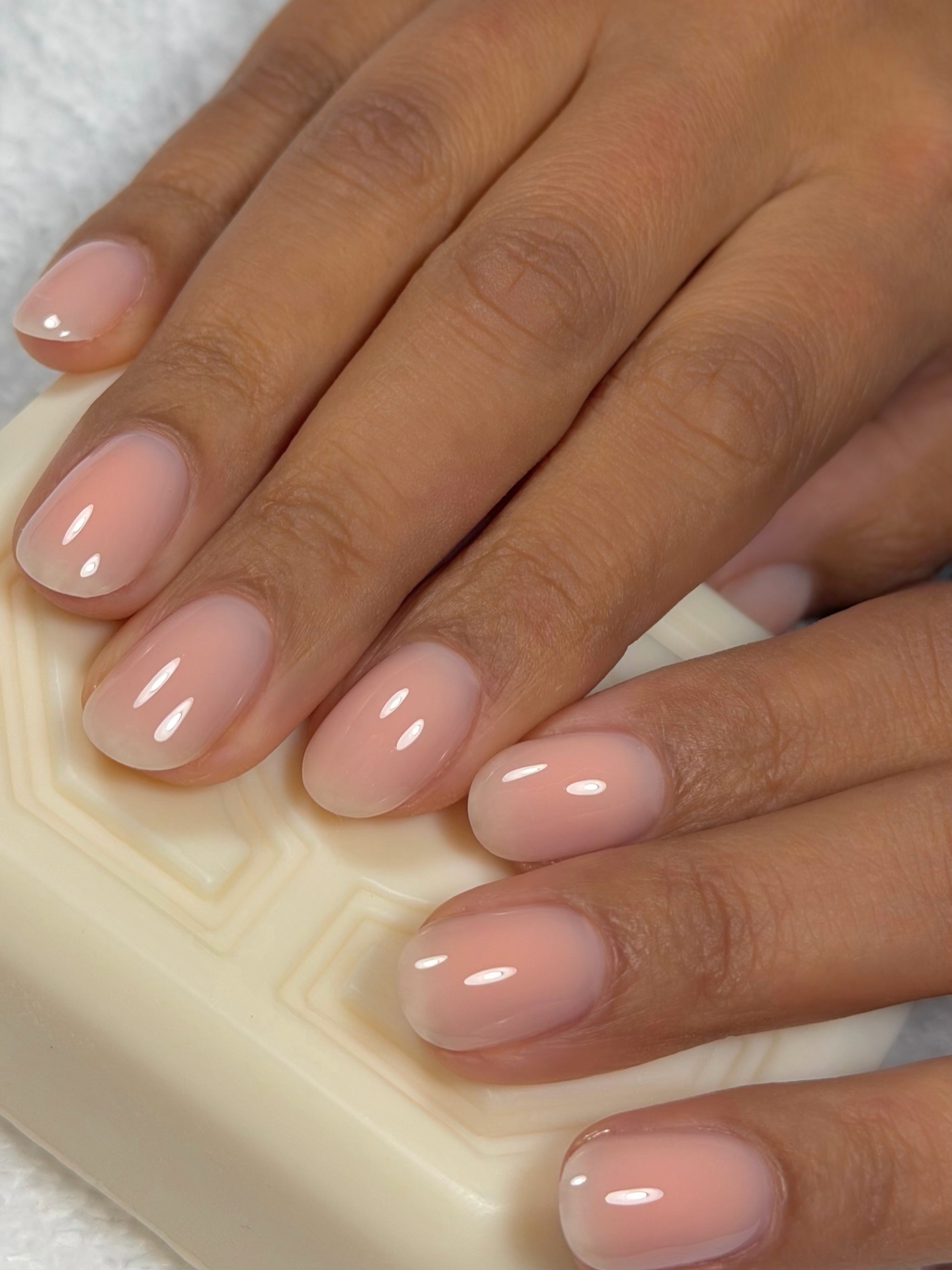 A photo of hands holding a bar of soap painted with a sheer peach nail colour shade