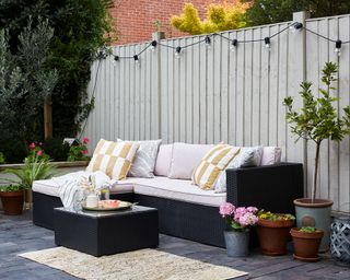 Pale colored fence strung with festoon lights in an airy seating area