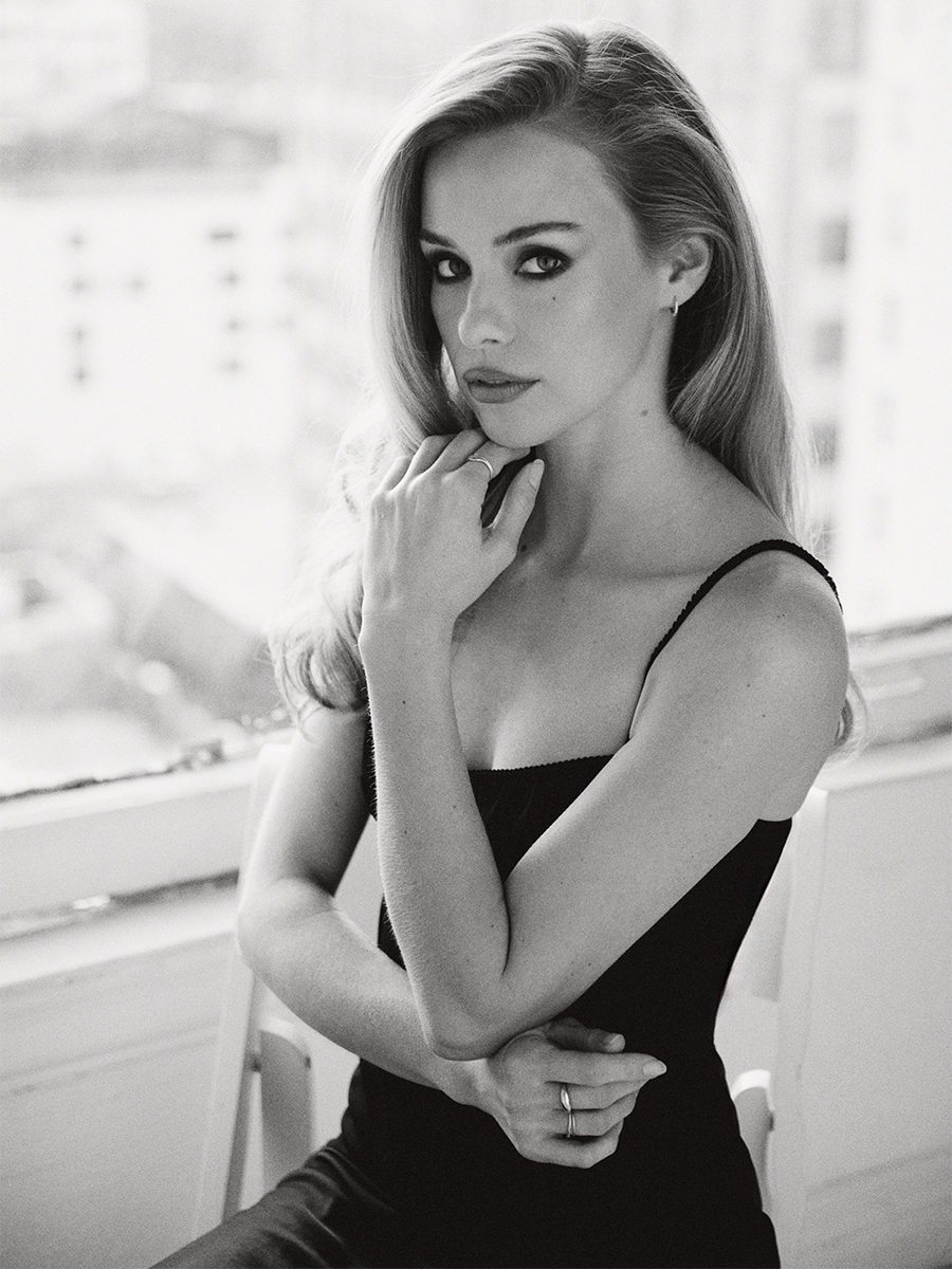 Black and white portrait of Elle Chapman sitting in a chair wearing a black top and skirt.