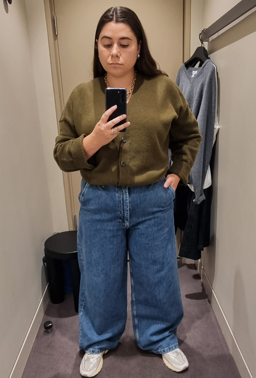 A woman wears blue wide-leg jeans and a green cardigan