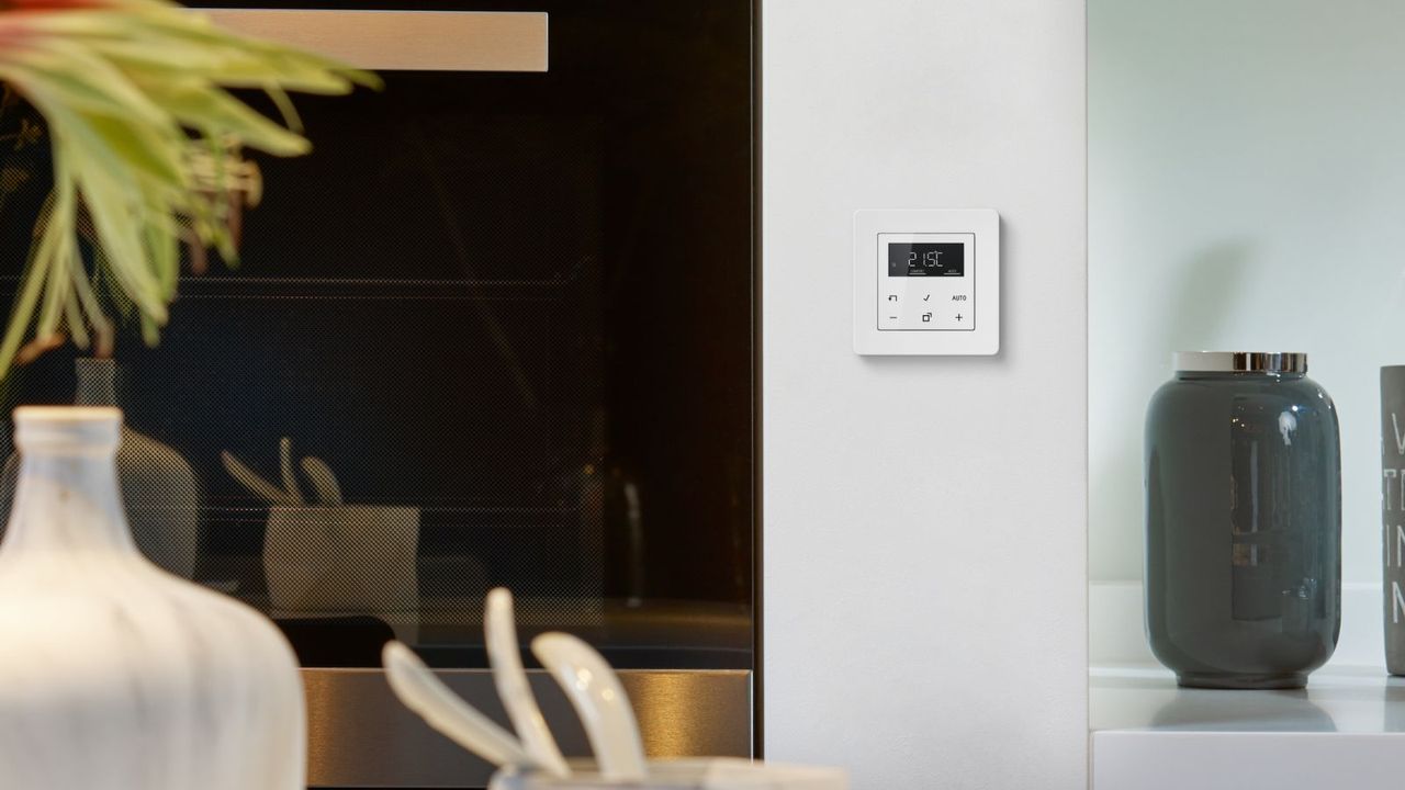 A small white smart thermostat on a wall in a kitchen