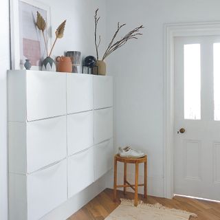 All white hallway with white shoe storage on wall.