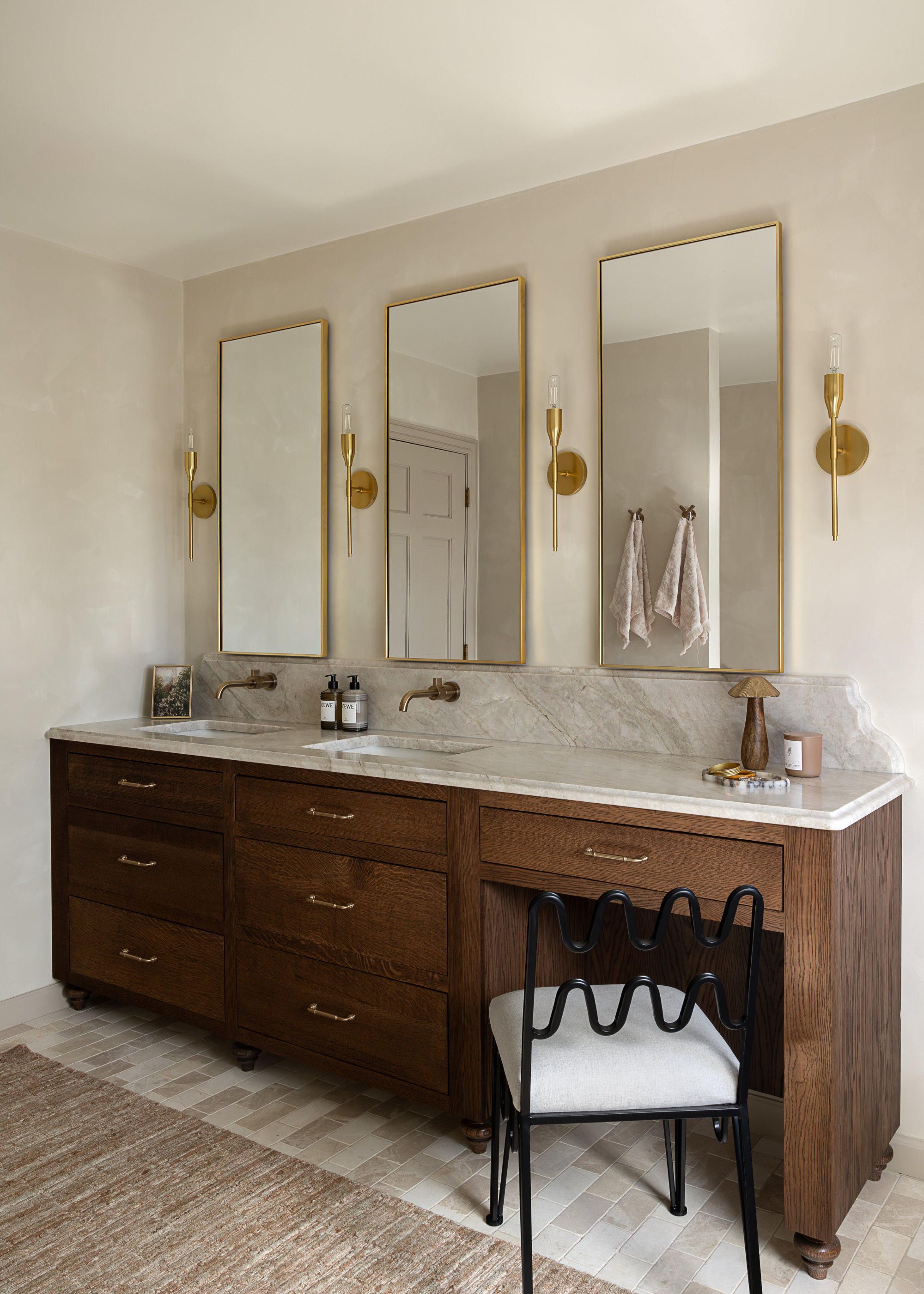 a modern, neutral, airy bathroom with wooden cabinetry and marble surfaces, with three gold mirrors and golden accessories