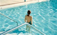 Woman standing in a swimming pool with her back to the photographer