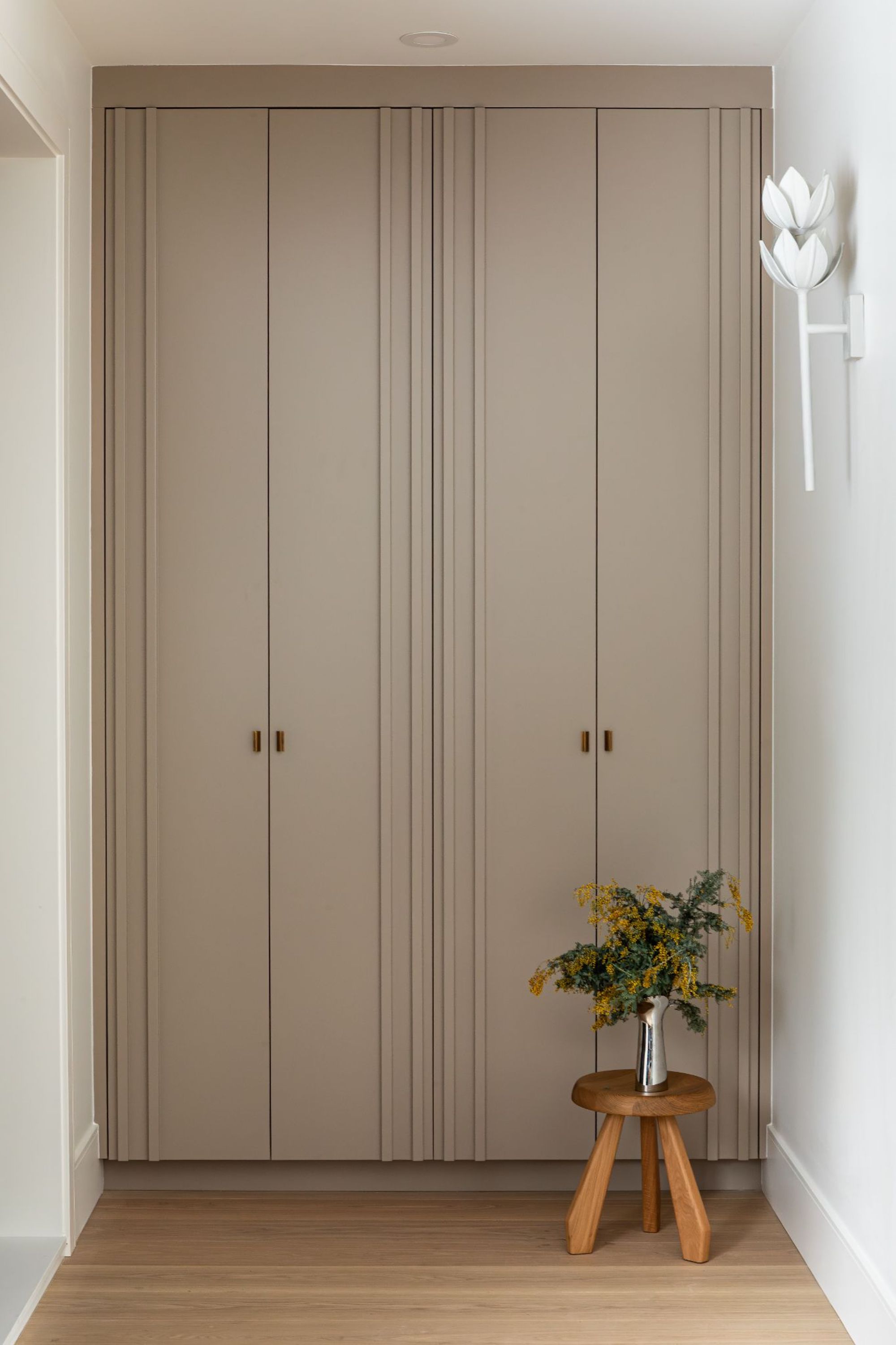 A view of two tall, beige cupboards with a small wooden stool to the right.