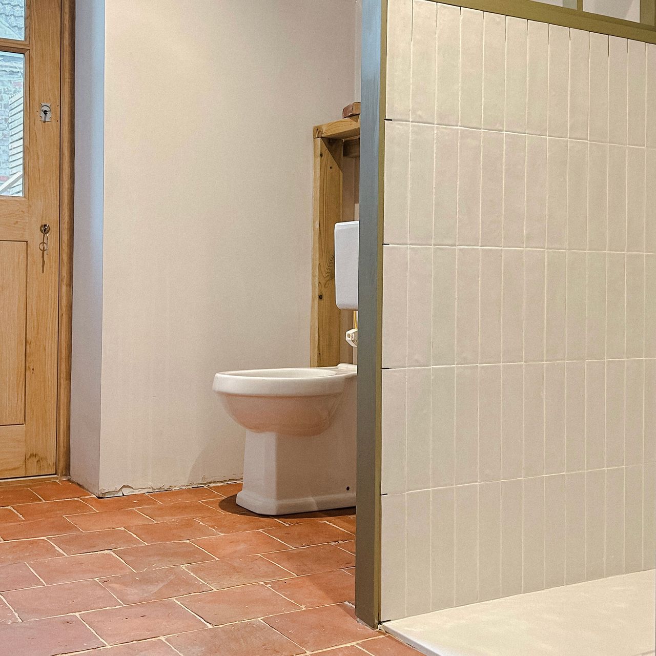 Bathroom terracotta tiled floor leading into shower enclosure tiled in pale green rectangular tiles