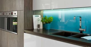 white kitchen with blue glass splashback highligted by under-cabinet strip lighting to suggest a cheap home improvement