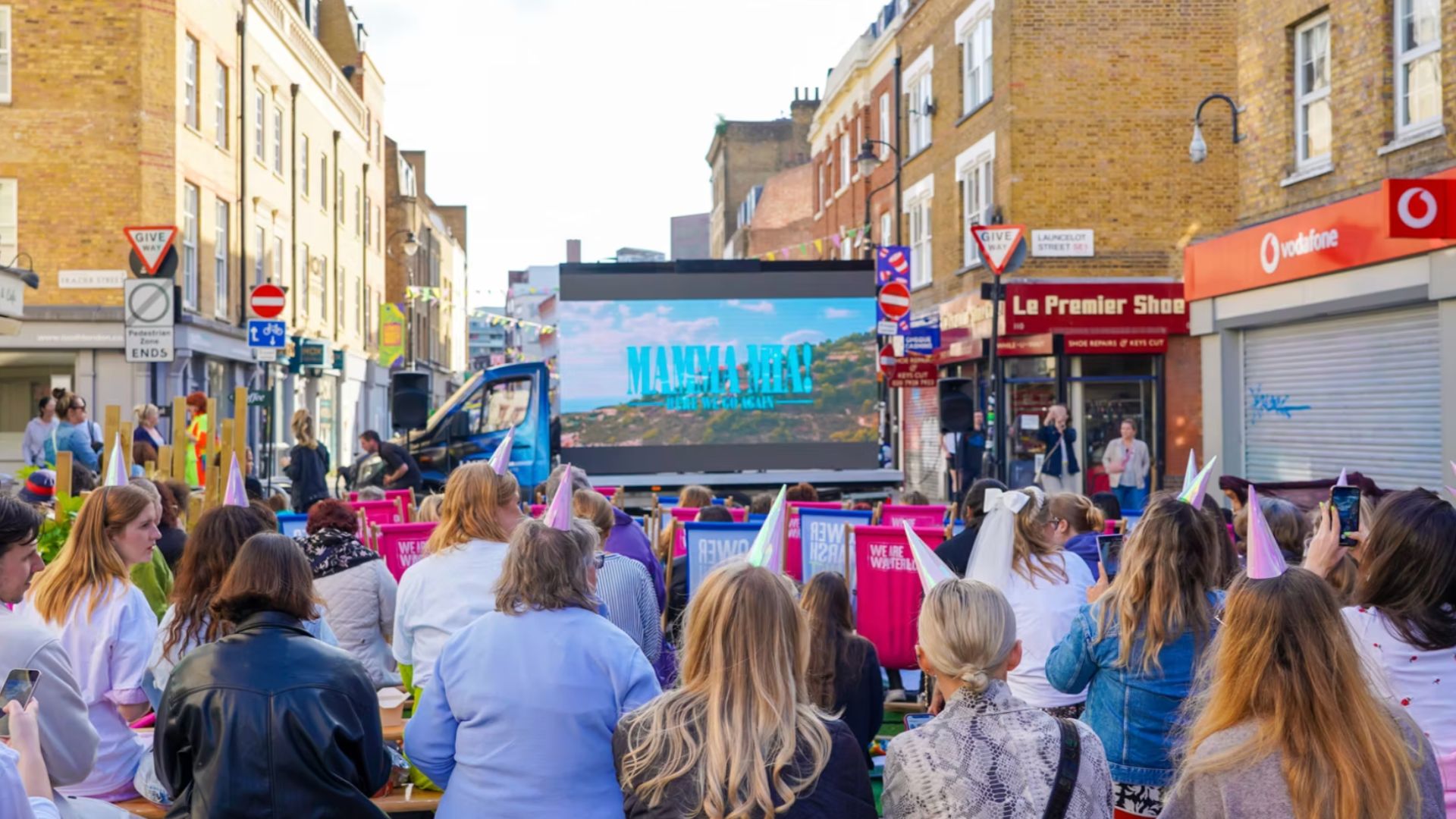 an image of the outdoor cinema with a crowd of people seated on deck chairs in front of a big screen showing Mamma Mia