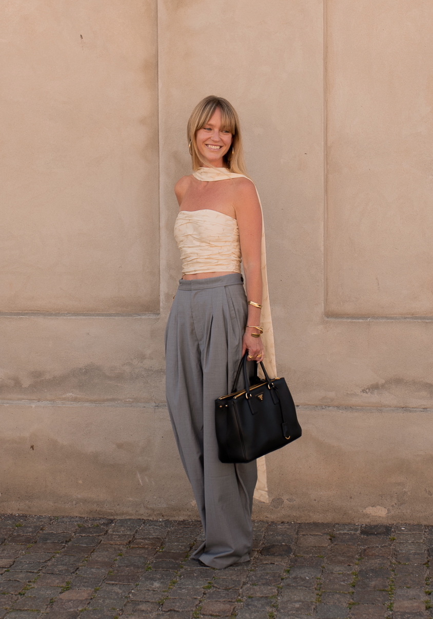 a woman at copenhagen fashion week wearing a cream tube top, scarf, and gray pants