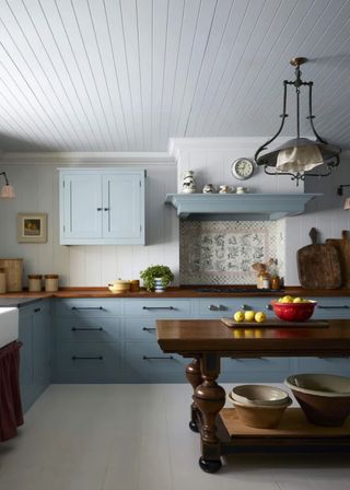 beadboard kitchen cabinets in blue and walnut with a large wooden island/table in the middle of the kitchen. A chic pendant light hangs above the table.