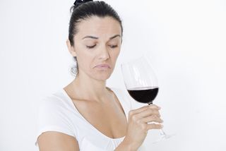 A woman stares at a glass of wine.